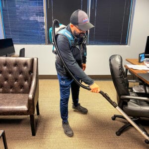 Janitor using a backpack vacuum on commercial carpet flooring