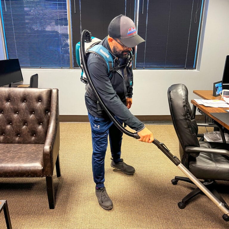 Janitor using a backpack vacuum on commercial carpet flooring