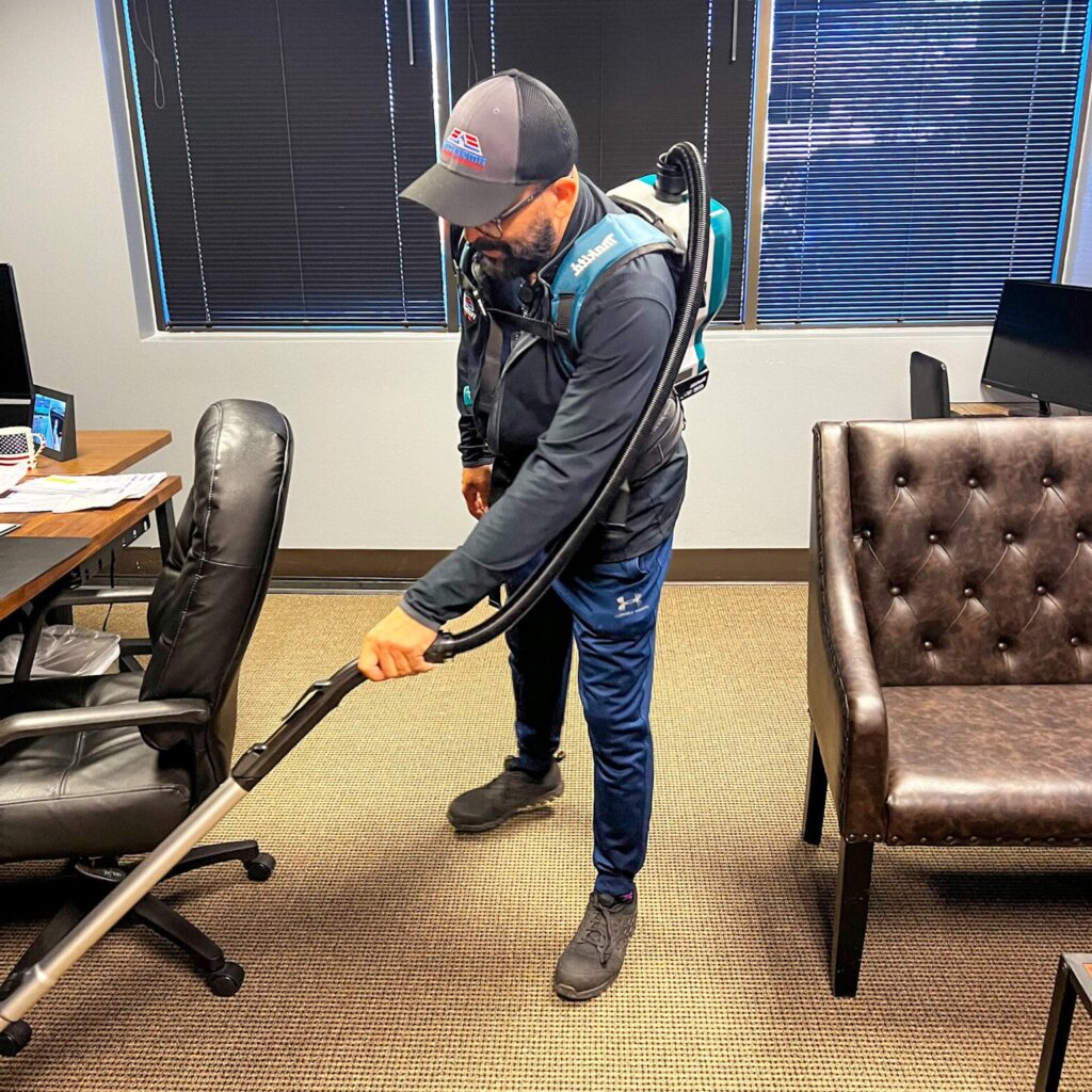 Janitor using a backpack vacuum on commercial carpet flooring
