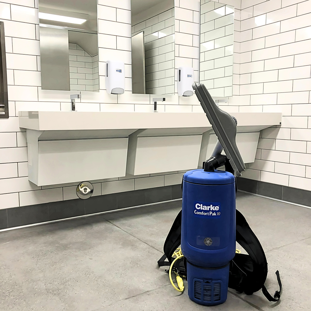 Backpack vacuum positioned on the bathroom floor of a commercial facility