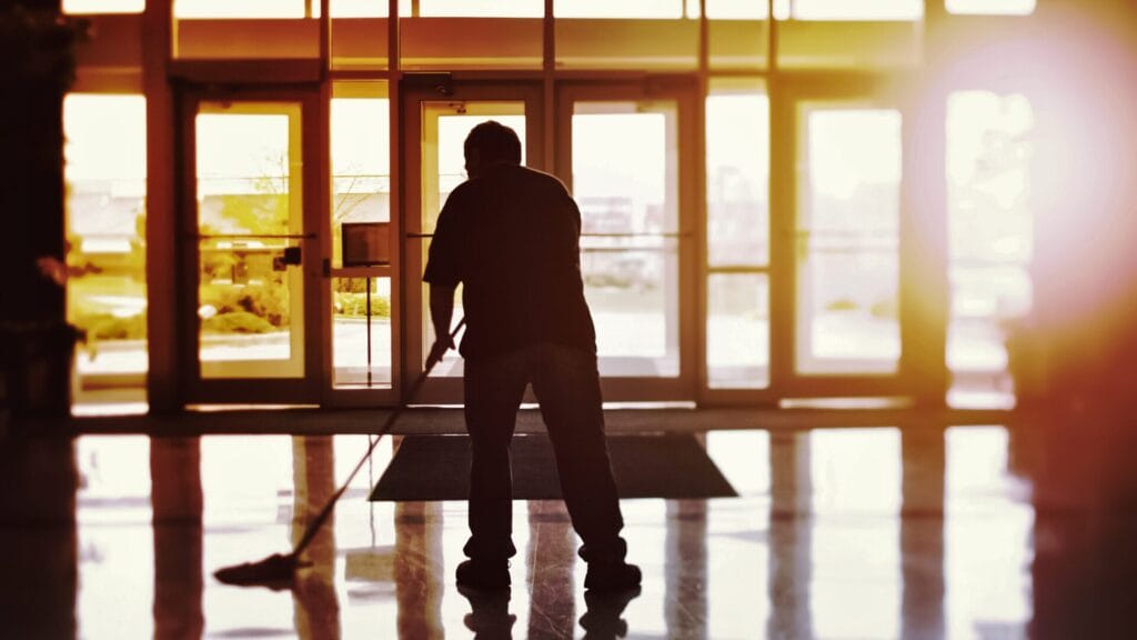 Silhouette of a cleaner mopping a floor against a sunset background, symbolizing dedication of cleaning services