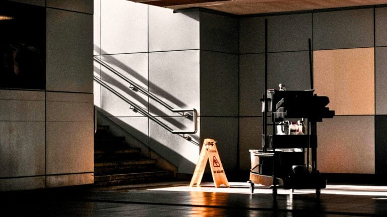 Janitorial cart with cleaning supplies and a wet floor sign during facility closing hours.