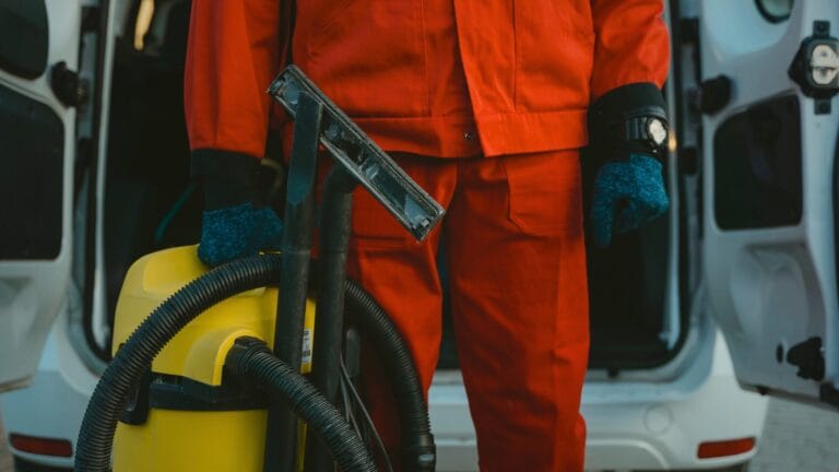 Commercial cleaner holding a vacuum with a cleaning van in the background, ready for outsourced janitorial services.