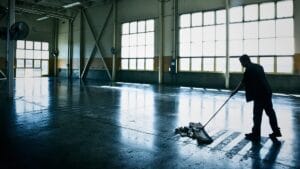 Industrial cleaning worker mopping a large facility floor to maintain cleanliness and safety standards.